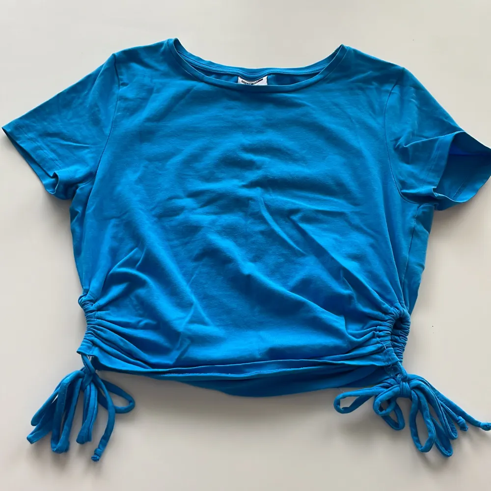 Jättesöt, blå tröja med snören som man kan knyta på sidan . T-shirts.