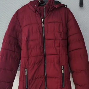 Höst/vinterjacka lång - Lång jacka. Färg är vinröd/oxblodsfärgad. Sparsamt använd så hel och fin. Funkar bra både höst och vinter. Inte jättetjock men håller värmen bra en kall vinter