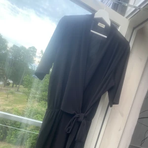 By malene Birger - Svart klänning i följsamts material. Bringad med knytsetslj i midjan. 