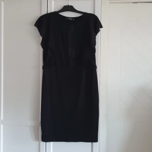 Klänning - Svart klänning, till knäna, volang på axlarna, lite brodyr längst fram på bröstkorgen. 
