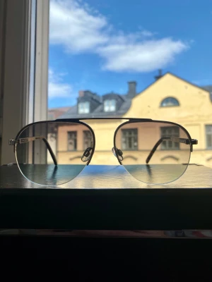 Smarteyes – solglasögon – De la Sol - Smarteyes – De la Sol H488  Knappt använda i väldigt fint skick (utom en liten repa på det högra glaset).  Pilotbrillor i metall, bågar i acetat.  Glasbredd: 55 mm. Bryggstorlek: 15 mm. Skalmlängd: 145 mm.  Hämtas i Stockholm, Vasastan. Eller skickas.