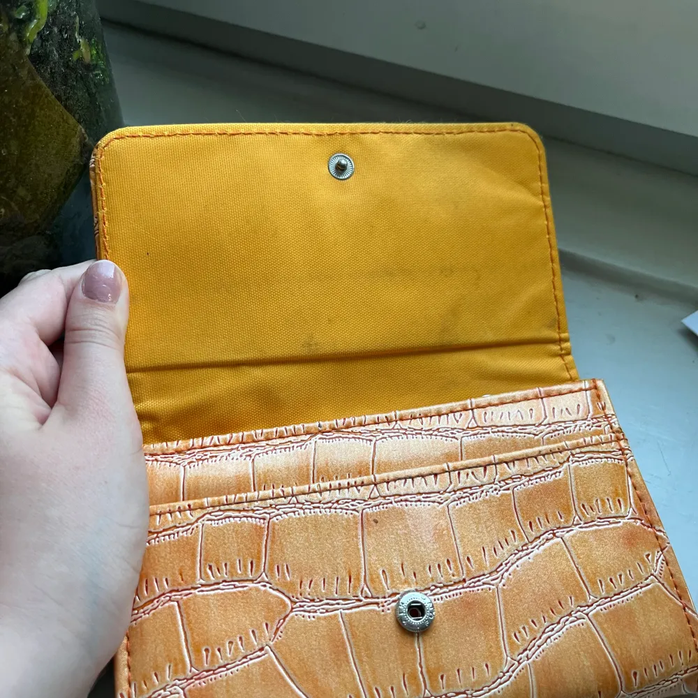 En orange plånbok som jag inte var vart den kommer ifrån. Den har en silver ditalj där framm och har mönster.  Kommer sälja pga inte använder lika mycket som förut! . Väskor.