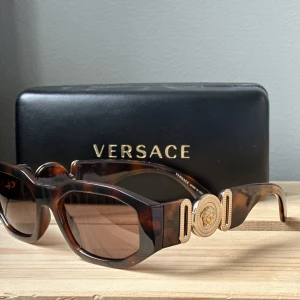 Versace Solglasögon med gulddetalj - Versace Solglasögon med gulddetalj. Använda sparsamt och alltid varit förvarade i case som kommer med. Köpte på Zalando 2020. Meetup Stockholm. 