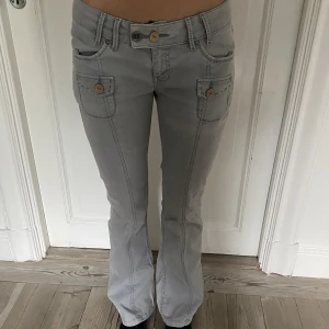 Lågmidjade jeans med detaljer  - Säljer jättesnygga jeans som är lite grå/blå med knappar och snygga detaljer från Levis. Midjemåttet är 35 och benlängden är 101. Det står 27/32 men jag har vanligtvis 24 eller 25 och de passar mig.