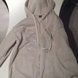 Kofta med luva  - En fin beige kofta med en glittrande fjäril 