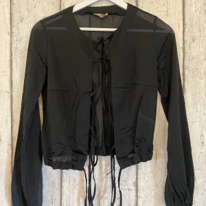 Svart blus - En svart genomskinlig blus som man knyter med snören i fram. 💝 Den har en resårbotten vilket ger den bra form.  Säljer då den ej kommer till användning.