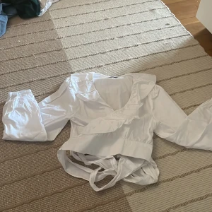 Blus - Vit blus med långa ärmar och omlott i midjan. Mycket fint skick, aldrig använd. Från NA-KD. Säljer för 100kr