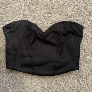 Svart bandaeu korsett - Svart bandaeu korsett i silke, från ginatricot i ett väldigt bra skick nästan aldrig använd inga defekter. Vid fler frågor/bilder skriv privat💗köparen står för frakt