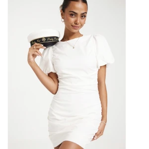 Vit studentklänning - Fin vit klänning från Nelly, öppen rygg med två rosetter och puffärmar. Klänningen är slut i lager så väldigt eftertraktad. Nyskick då jag aldrig använt den! Perfekt till båda student eller en sommarkväll✨ Stl.38