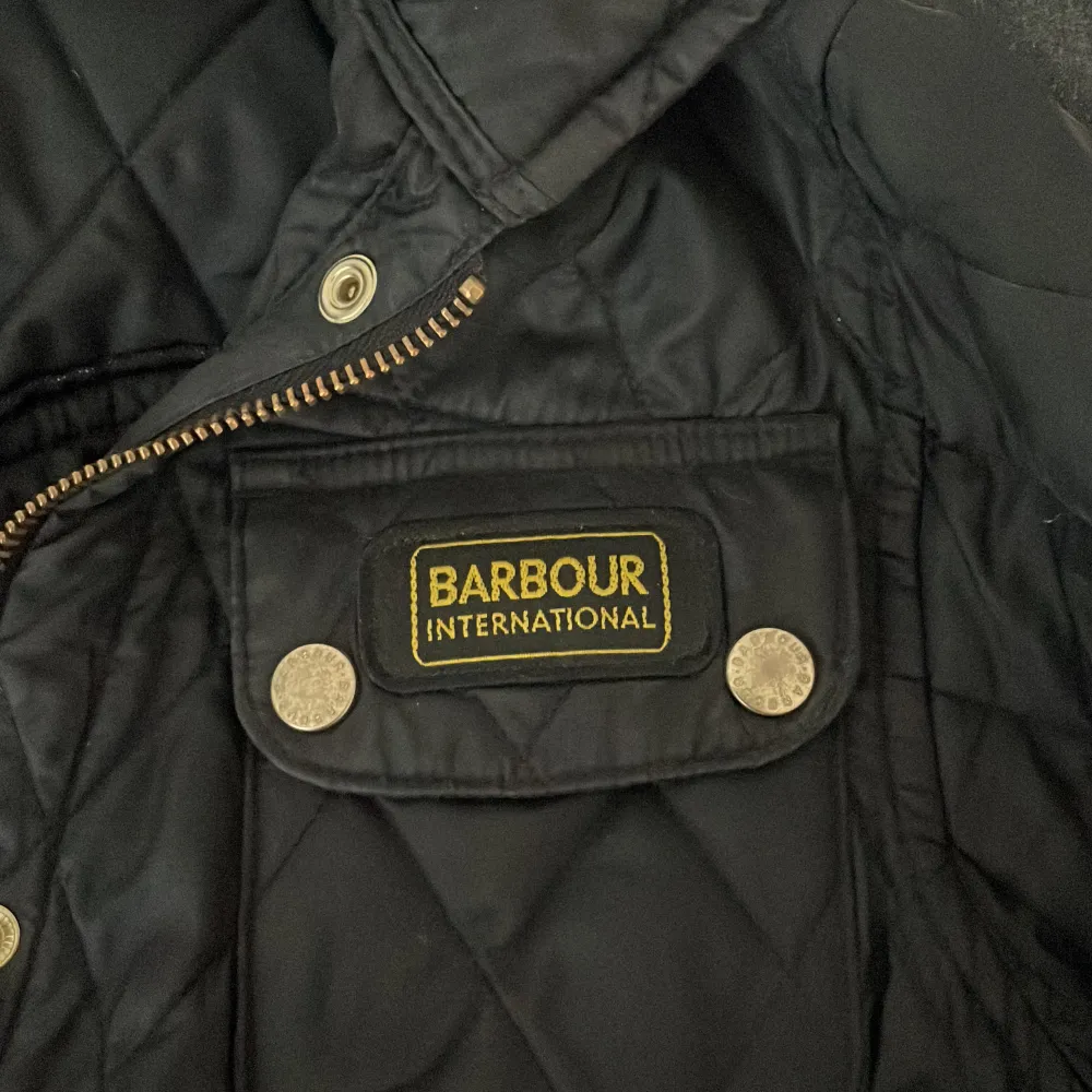 En svart äkta Barbour jacka som passar xs,s och m. Med ett bälte och tragkedjor vid händerna samt fyra fickor   . Jackor.