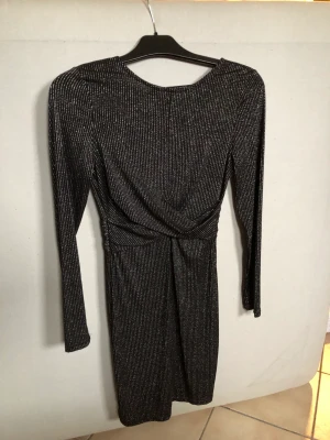 Silvrig/svart klänning storlek S från bubbleroom  - Långarmad silvrig/svart klänning i storlek S. Öppen rygg och dragkedja. Stretchigt material, gjord av 74% polyamid, 20% metallfibre och 6% elastan. Säljs då den inte passar längre. Använd några gånger, perfekt till nyår. Kommer från ett rökfritt hem.