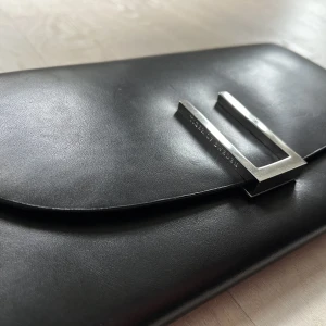 Tiger of Sweden handväska oanvänd - Väldigt fin och stilren svart clutch handväska från märket Tiger of Sweden. 22x12 cm.Helt oanvänd så den luktar fortfarande läder. Ord pris ca 1500kr Den är slutsåld i butikerna.  Den har fickor för kort och dragkedja för kontanter. Medföljer en dustbag. 