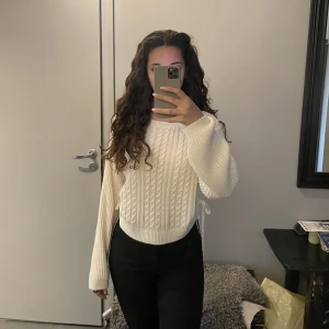 Vit stickad tröja  - En tunn creme vit stickad tröja från Nelly i storlek XS. Den Har justerbara sidor, som man kan knyta och blir en fin detalj. Tröjan är i mycket bra skick och är i måtten 53 cm (axelbredd) och 54 cm (längd).