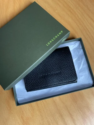 Longchamp mindre plånbok - Svart mindre plånbok från Longchamp. Mycket fint skick. Skinn. Kommer i ask. Stängs med knapp. Bra med utrymme för kort och lite lappar och sånt. 