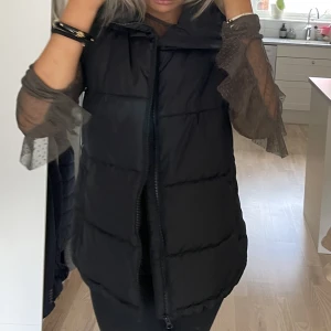 Täckjacksväst  - Svart väst som kan knytas i midjan om man vill. Använd Max tre gånger. 