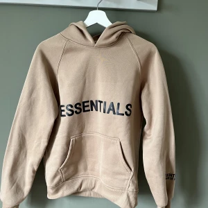 Essentials Hoodie hoodtröja - Hoodtröja med texten Essentials i en mörkbeige/ljusbrun färg. Inköpt i år och aldrig använd. Gosig och mjuk 🍂🤎 Storleken är M men den är liten i storlek, passar mer en S