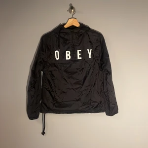 Obey jacka - Lite tunnare jacka med fodring och luva. Från märket OBEY och i storlek XS, för både tjejer o killar!