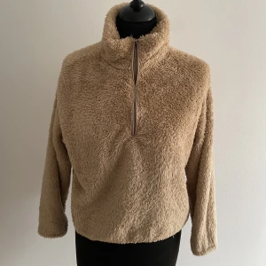 Kort fluffig tröja  - Kortare beige tröja i teddyfluff med 3/4 arm och dragkedja över bröstet så kragen kan justeras. Strl xs. Använd fåtal gånger