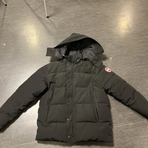 Canda Goose Jacka - Säljer min Canada Goose pga det är inte min stil längre har använt den i två år  En knapp är av längst ner på jackan och dragkedjan är lite knepig att dra men annars är allt i bra skick och känns som en ny skriv för fler bilder Storlek XL men känns som L