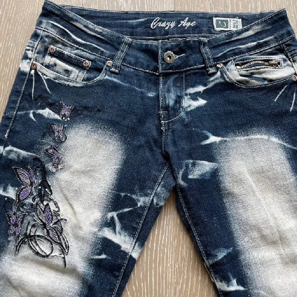 Snygga lågmidjade bootcut jeans från Crazy age med strass och tryck!! 2 fjärilar på baksidan och sex mindre på framsidan. Super bra skick förutom två nästan osynliga fläckar på framsidan ( se bild 1 ). Storlek EU 38, MÅTT - Midja-76cm, innerbenslängd-83cm. Jeans & Byxor.