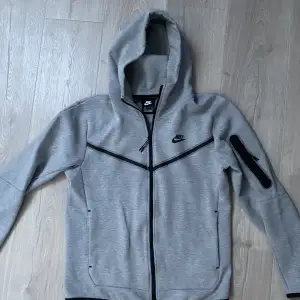 Grå Nike Tech Fleece, 9/10 Skick Använd kanske 10 gånger max, säljer den då den blev för liten. Nypris 1349 kr