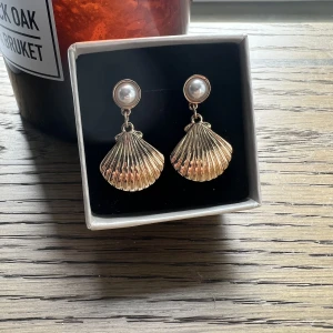 Örhängen  - Ett par fina pärlörhängen med en hängande guld-snäcka på. Väldigt fint skick. Vet tyvärr inte vilket märke det är då jag fick dem i present.