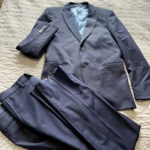 Kostym set (kavaj och byxor) dressman  - Lyxig marinblå kostym set som är super elegant. Kostymbyxor (st 33/32) och kavaj (st. 48) använd i fåtal timmar. Slim fit i modellen. Inköptes från Dressman. Finns fler bilder vid önskemål! Ordinariepris  2500.  