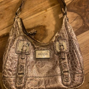 Guess väska - Medelstor Guess väska i brun/beige ormskinn med silverdetaljer. Säljer då den inte kommer till användning. Köpte på plick för 300kr och säljer för 150kr🤍