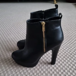 Skor - Svarta högklackade skor med svart dragkedja på insidan och guldig dragkedja på utsidan. 