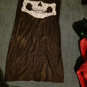 Svart tubhalsduk med tryck  - Kanterna är inte insydda av någon anledning, se bild. Materialet är nåt slags halv-stretchig polyester-material. Typ oanvänd.