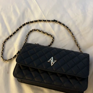 Svart Handväska med guld detaljer  - Svart handväska med guld detaljer, fick av en vän men har ej andvändt då jag ej passar i guld, bra kvalitet, ser ut att vara läder, går att ha både som lång väska och som kort Axel väska 