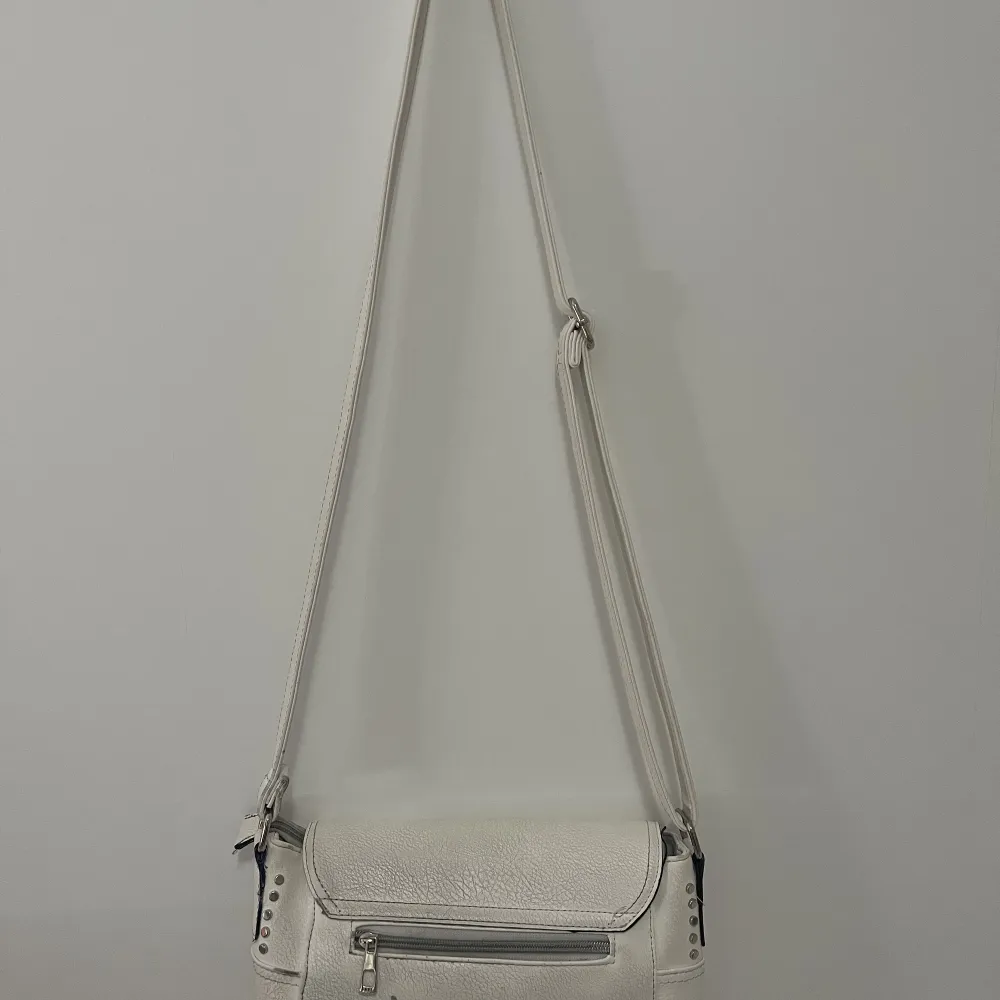 En vit väska i ungefär 25 cm i bredd, 20 cm hög och 10 cm djup.  Använts i ett år och är då i begagnat skick med små defekter i fake lädret, kedjor funkar.  Köpt från Gekås  🌟🫶🤍. Väskor.