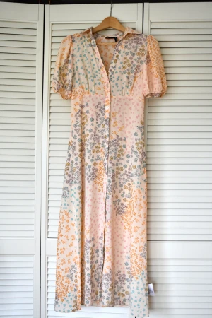 Blommig tea-klänning i skjortmodell - Nypris: 489kr Aldrig använd, tiden för returnering gick ut. Midiklänning, normal i storleken, går till strax ovanför ankeln. Knäppning framtill och krage. Puffga ärmar.