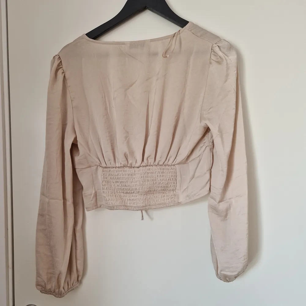 Beige satinblus med snörning. Storlek L men liten i storleken. Passar storlek S och M. Endast använd en gång. Köpt på Asos. Nypris 289 kr.. Blusar.