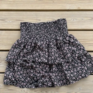 Blommig kortkjol - Fin kortkjol med lila blommor, använd några gånger, men ser absolut inte sliten ut, storlek 140, men man kan vara lite längre 