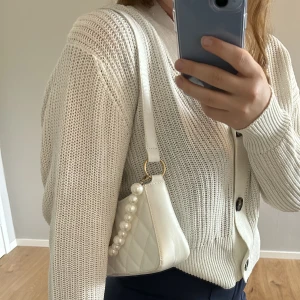 Väska - Vit väska i läderimitation. Pärlbandet går att plocka bort.