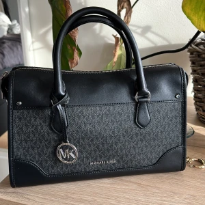 Michael Corse väska - Säljer en helt nyinköpt och oanvänd Michael Corse väska i modellen: Harrison Medium Logo Satchel, i färgen: black  