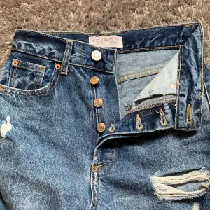 Jag säljer dessa fina mörkblåa jeans för att dom aldrig kommer till användning. Dom har ett hål på högerknä och en liten glipa med vit tråd uppe på vänster höft. Så fina och är i mycket bra skick. Dom är highwaist och har knappar istället för dragkedja. 