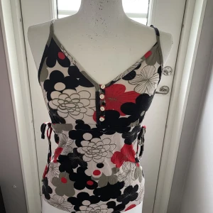 Söt blommig topp - Knyt på sidorna och knappar på framsidan. Justerbara band. 