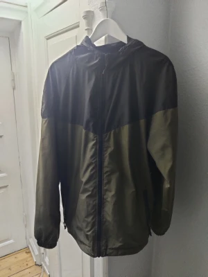 Vindjacka - Snygg vindjacka i färgerna militär grön och svart. Vindjackan är i ett gott skick då den inte använts många gånger.