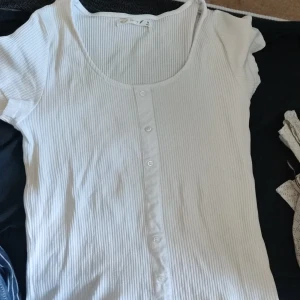 Vit ribbad tshirt  - Vit ribbad tshirt med knappar som ej går att öppna i storlek medium i fint skick 
