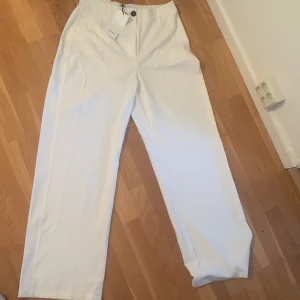 Vita kostymbyxor - Helt oanvända vita kostymbyxor från bershka med lappen på! Perfekt till studenten eller annat! Bra passform, säljer de pågrund av att det blev försent för att lämna tillbaka de. Storlek 40, nypris var ungefär 400kr