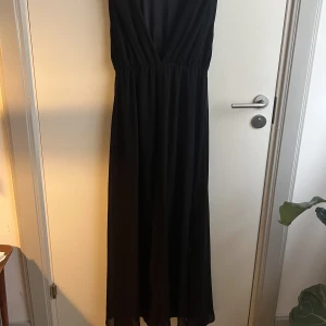 Svart klänning  - Svart lång klänning med slits och elastisk midja. Öppen i ryggen. 