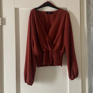 Blus - Rost-röd i färgen, jag har satt en säkerhetsnål för att begränsa v-ringningen men går givetvis att justera.