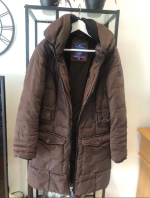 Tom Tailor jacka stl. S - Säljer en brun lång jacka i storlek S. Märket är Tom Tailor. Härligt material, varm och go. Bra kvalite. Mycket bra skick!! Många små detaljer med smarta funktioner. Samfraktar gärna. Säljer pga stor garderobrensning. Kika gärna på mina andra annonser:)
