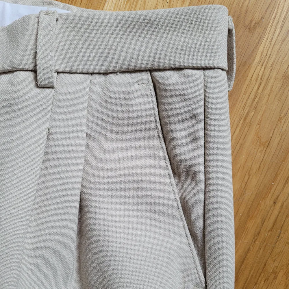 Kostymbyxor i grovt tyg med pressveck och fickor fram och bak. Jag har lagt upp dem så de är lite kortare och har därför vecken längst ner på benen. Högmidjade. Längd 95 cm.. Jeans & Byxor.