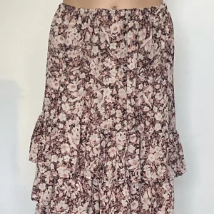 Brun/rosa Blommig kjol  - Jättefin brun sommarkjol, med rosa blommor och volanger. Var från början en klänning som jag har sytt om, finns därför spår av sömmar :) Har därför ingen storlek, men skulle säga S