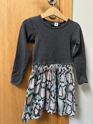 Molo klänning 98/104 - Molo klänning - grått liv med mönstrad kjol. Använd ett fåtal gånger, bra kvalitet, inga fläckar eller hål. 