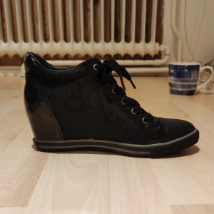 Modesneakers med liten klack. - Blanka, svarta modesneakers med snörning på en liten klack.  Lite använd men i mycket fint skick.  Skorna är väldigt bekväma.