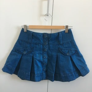 Jeanskjol - Jeanskjol från märket George, med knappar hela vägen och veckad nertill. Min systers gamla i jättefint skick, perfekt till sommaren! Står ingen storlek men detta är måtten: midja ca 34,5 cm, längd 33 cm. Skriv för fler bilder!